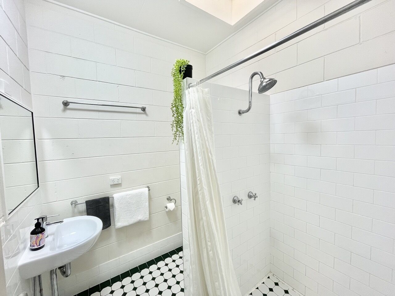 A bathroom with a white sink, a towel rack, a shower with a glass door, and a black and white tiled floor.