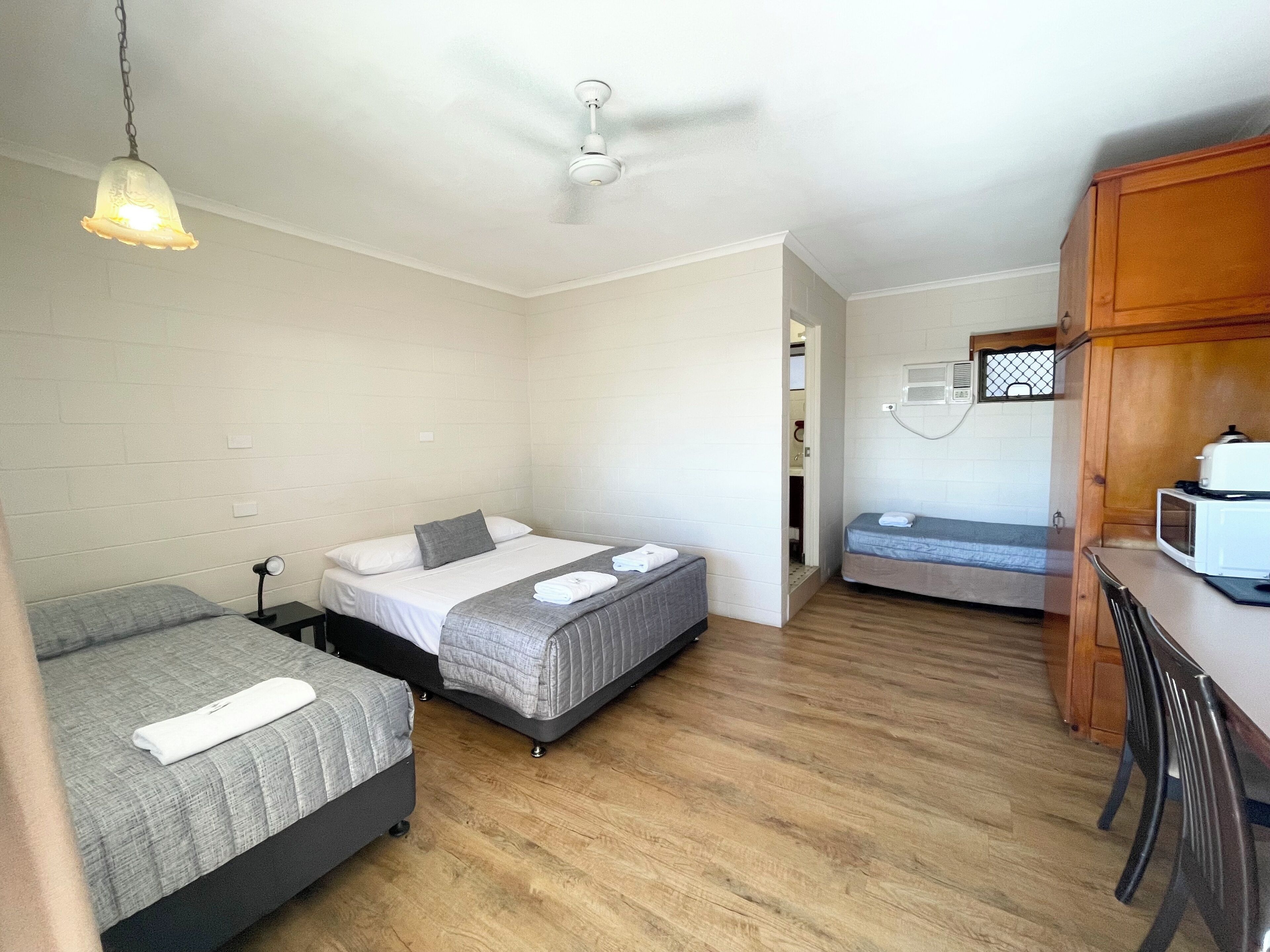 A compact room with two beds, a kitchenette, and a ceiling fan.