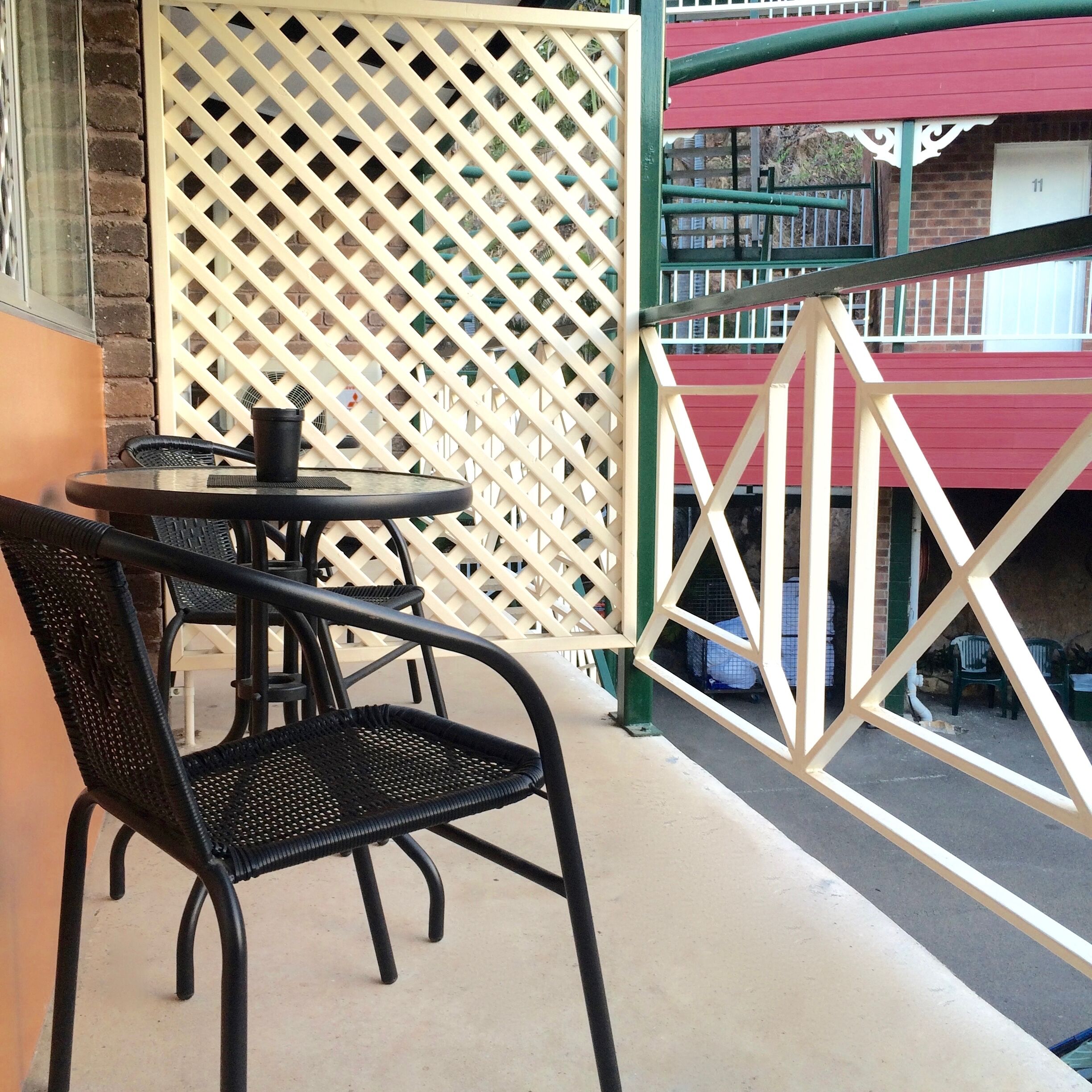 A balcony with a lattice fence, a table with chairs, and a red building in the background.