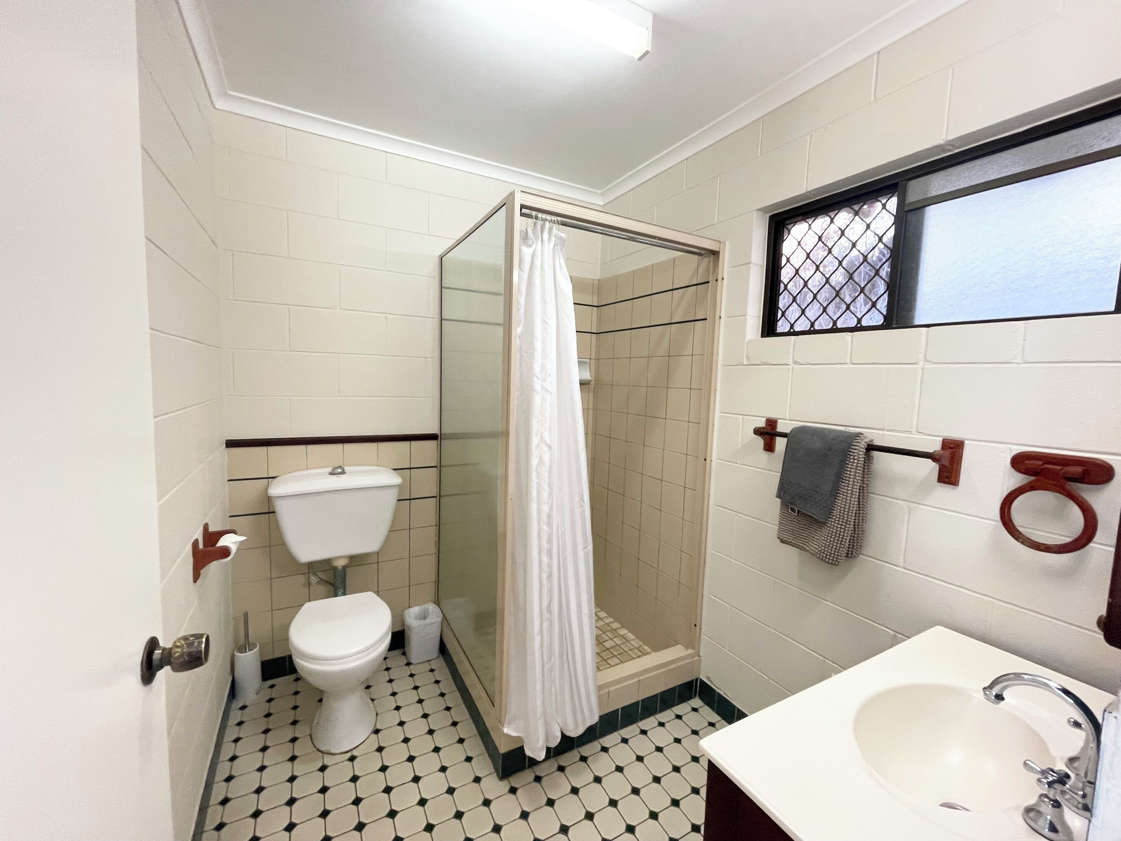 A bathroom with a toilet, a shower with a curtain, a sink, and a window with a metal grid.