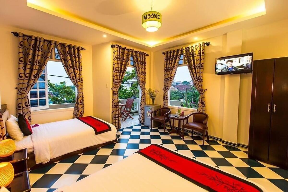 A hotel room with two beds, a checkered floor, a TV, a balcony, and a view of greenery.