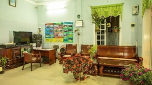 A living room with a wooden sofa, chairs, a TV, a desk, and a bulletin board with travel information. - Moon's Homestay (Da Nang)
