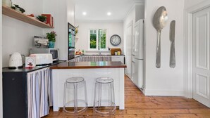 A modern kitchen with white cabinetry, a wooden countertop, and two clear stools. - 65 Main Daylesford - Hepburn Springs (Hepburn Springs)