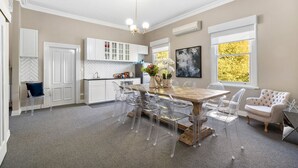 A spacious kitchen with white cabinets, a wooden dining table, and clear chairs. - 65 Main Daylesford - Hepburn Springs (Hepburn Springs)