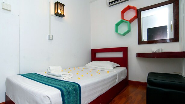 A neatly made bed with a white and teal bedspread, a red headboard, and a small bedside table with a mirror above it. - Agga Youth Hotel (Yangon)