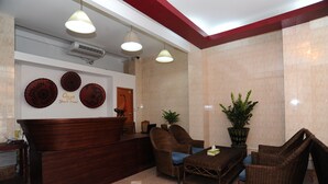 A reception area with a wooden reception desk, three wicker chairs, a small table, and a potted plant. - Agga Youth Hotel (Yangon)