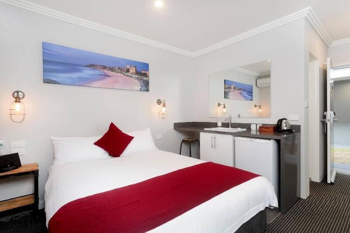 A hotel room with a bed, a desk, a mirror, a sink, and a door leading to a balcony.
