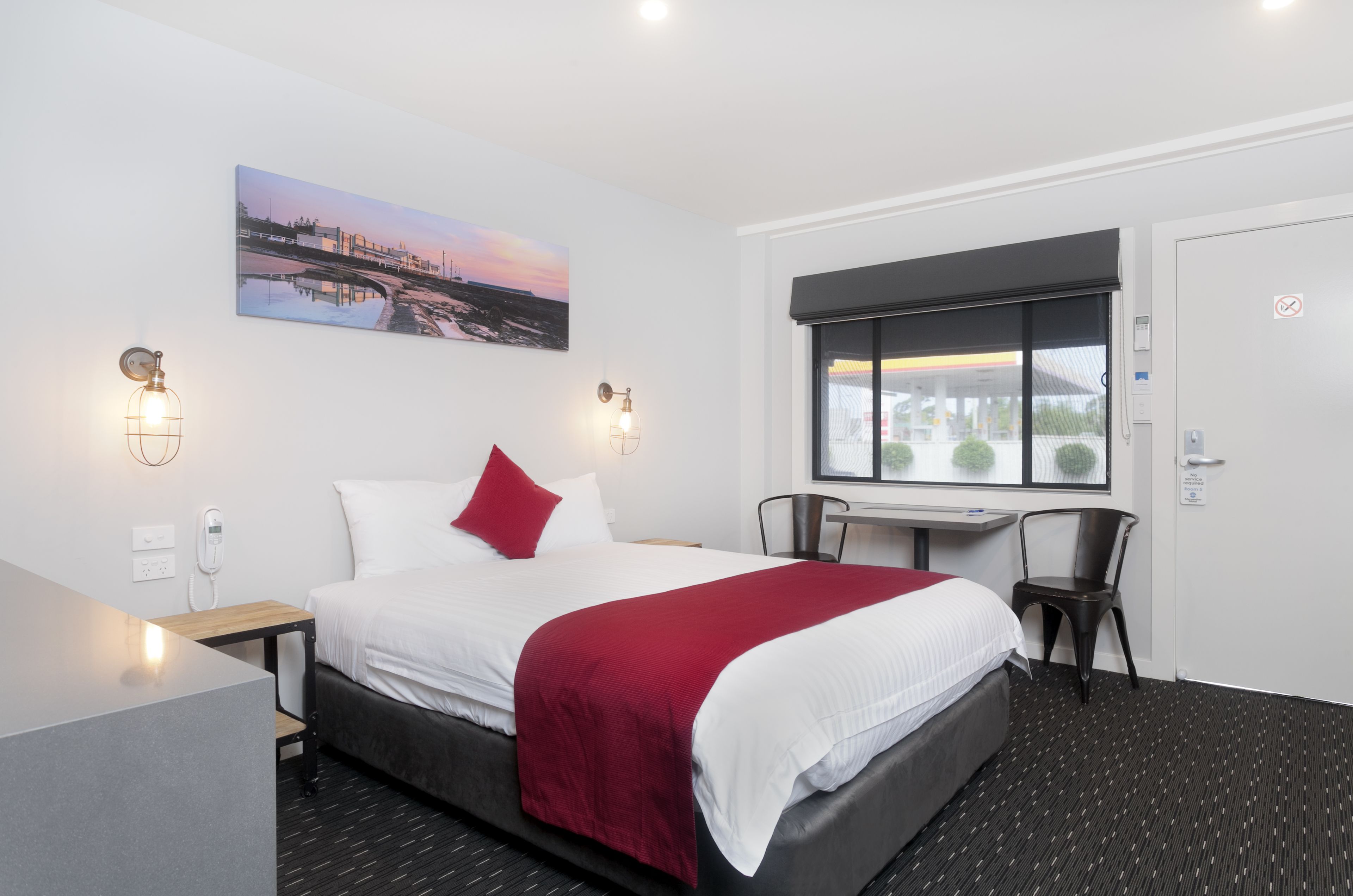 A hotel room with a bed, a desk, a chair, a window, and a painting on the wall.