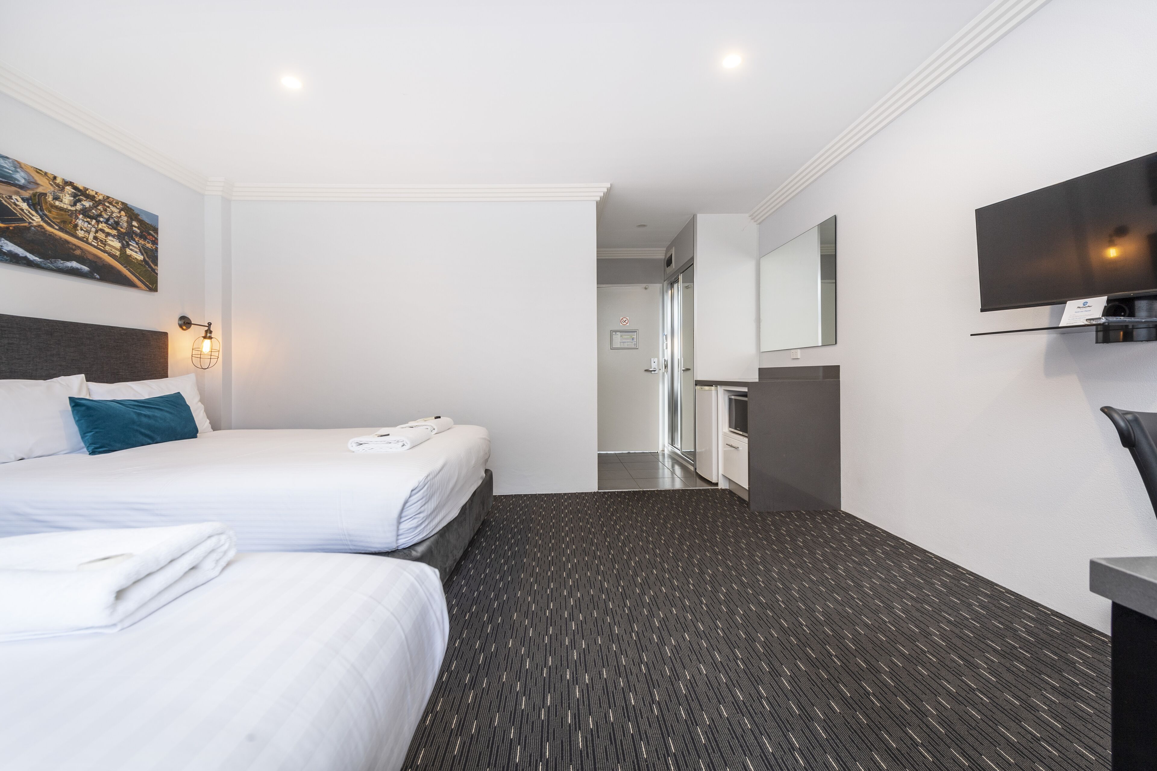 A hotel room with two beds, a large mirror, a flat-screen TV, and a carpeted floor.