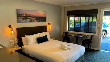 A hotel room with a bed, bedside lamps, a desk, a chair, a window with a view of a car, and a painting on the wall.