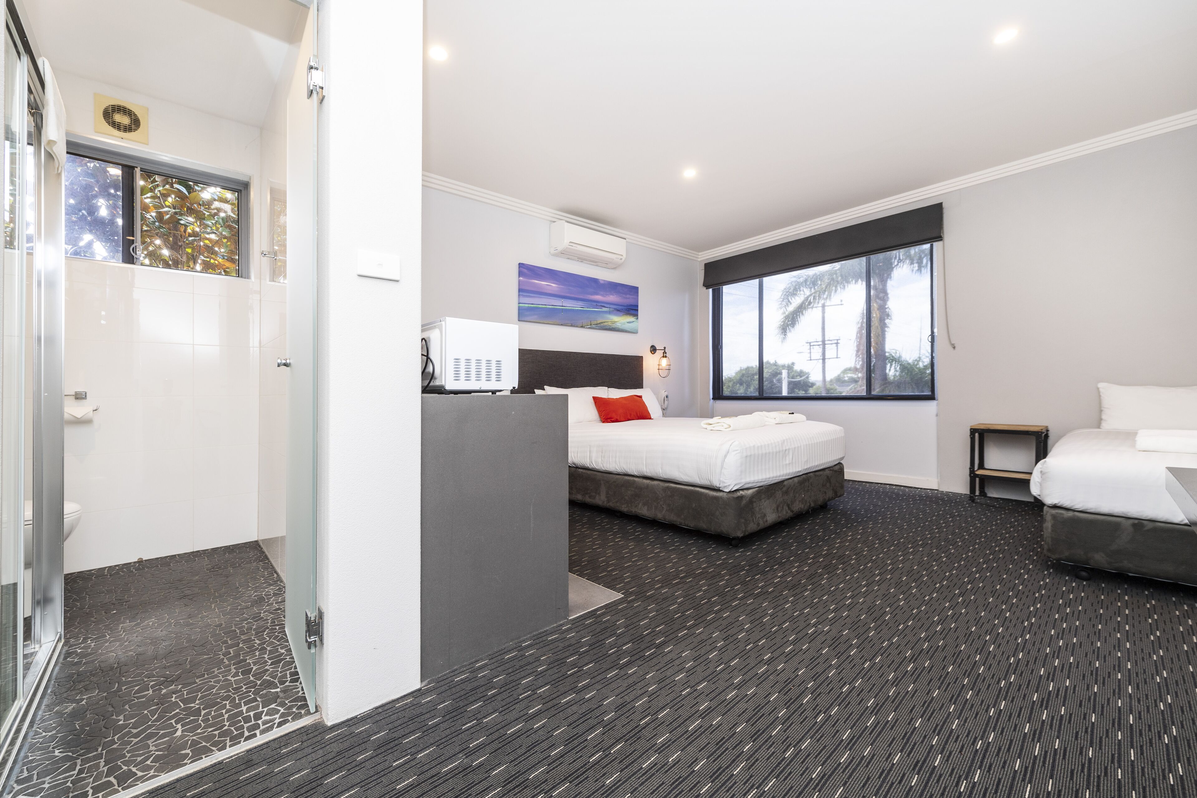 A modern hotel room with a bed, a desk, a small table, and a large window.