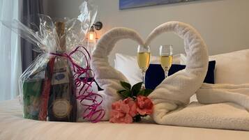 A neatly made bed with two white towels shaped like hearts, a bouquet of pink flowers, and two glasses of champagne.