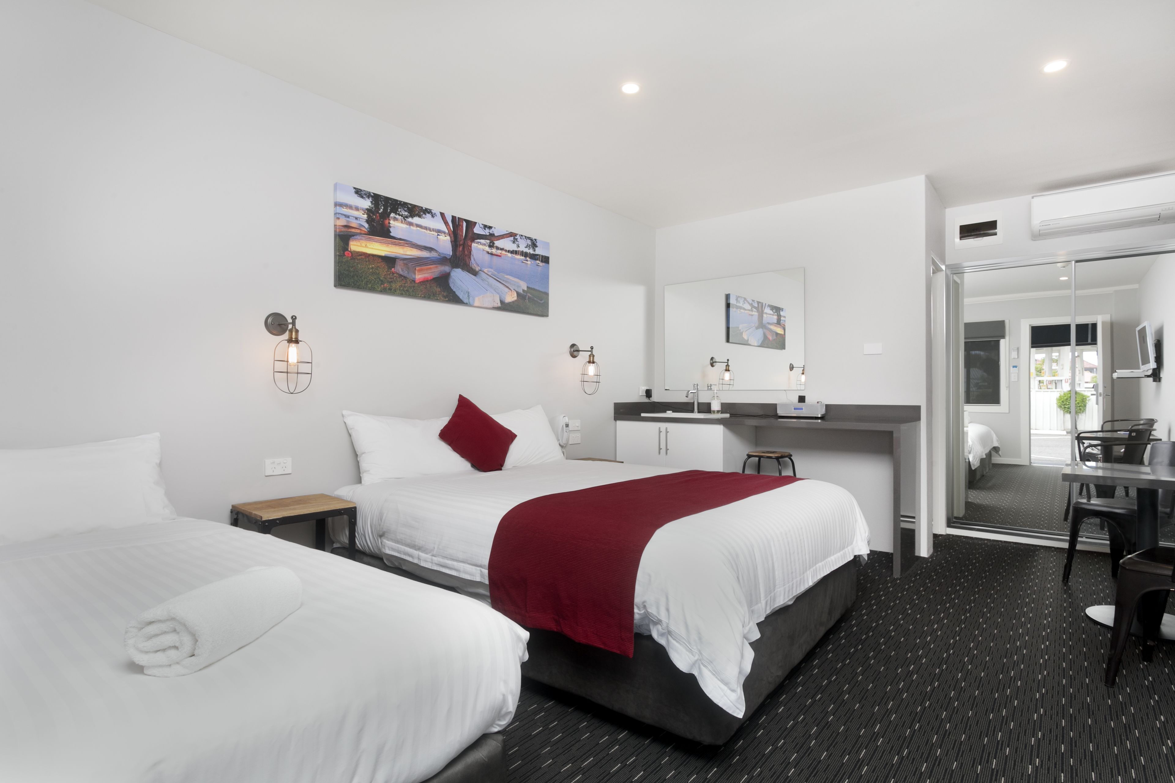 A hotel room with two beds, a desk, a chair, a mirror, and artwork on the walls.