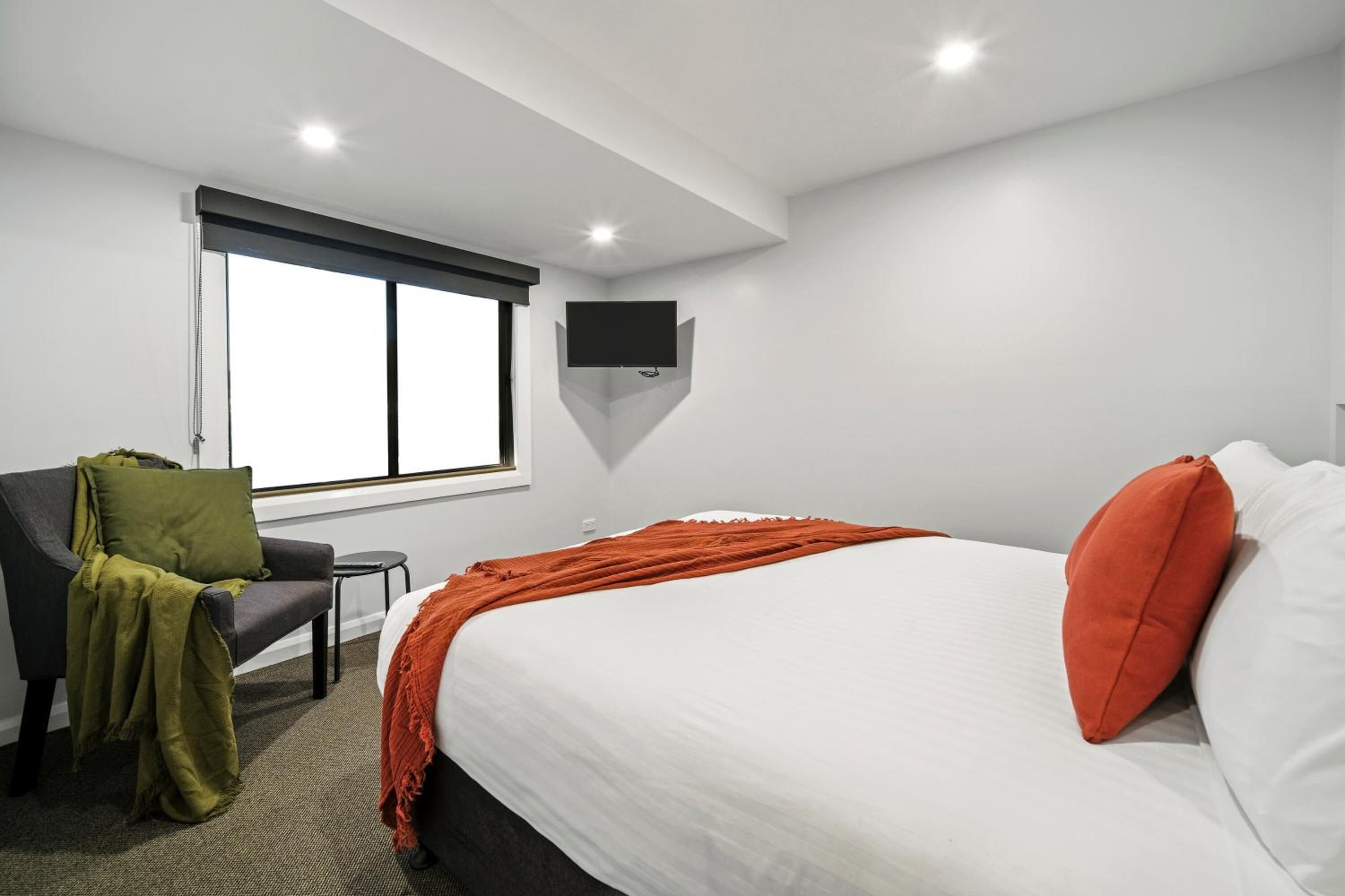 Quarto de hotel com cama, uma cadeira, televisão fixada na parede e janela.