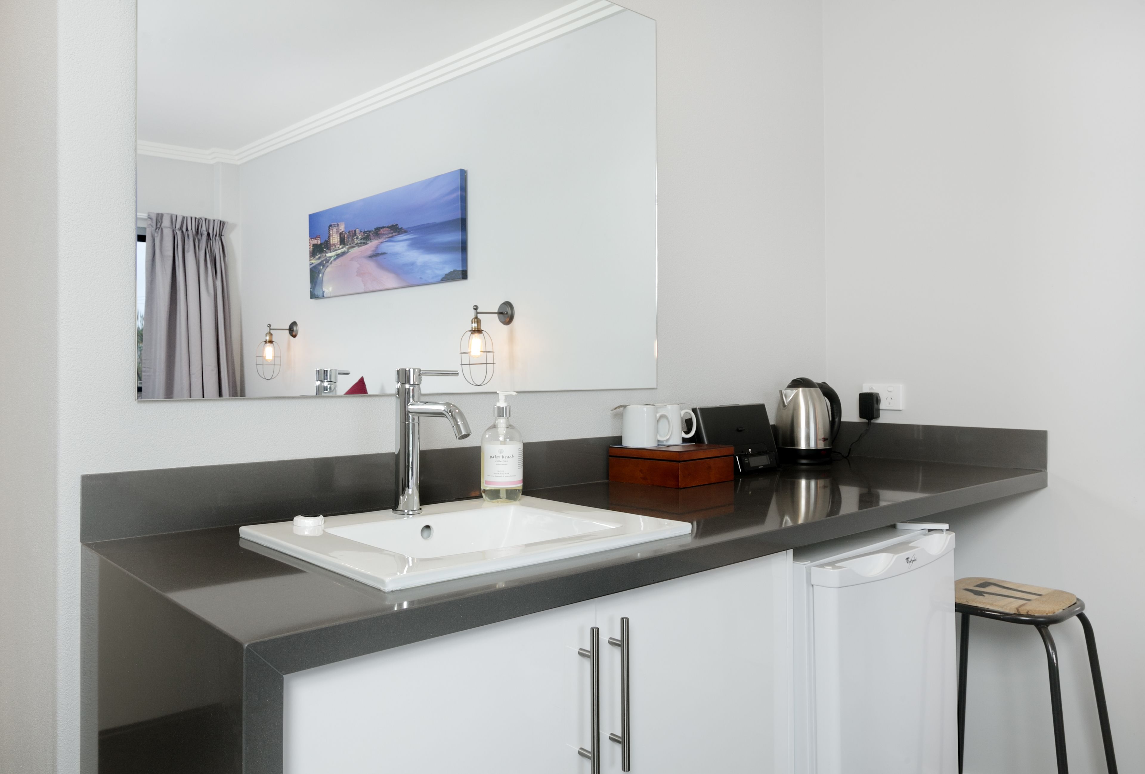 Une salle de bain moderne avec un grand miroir, un lavabo blanc et une machine à café.