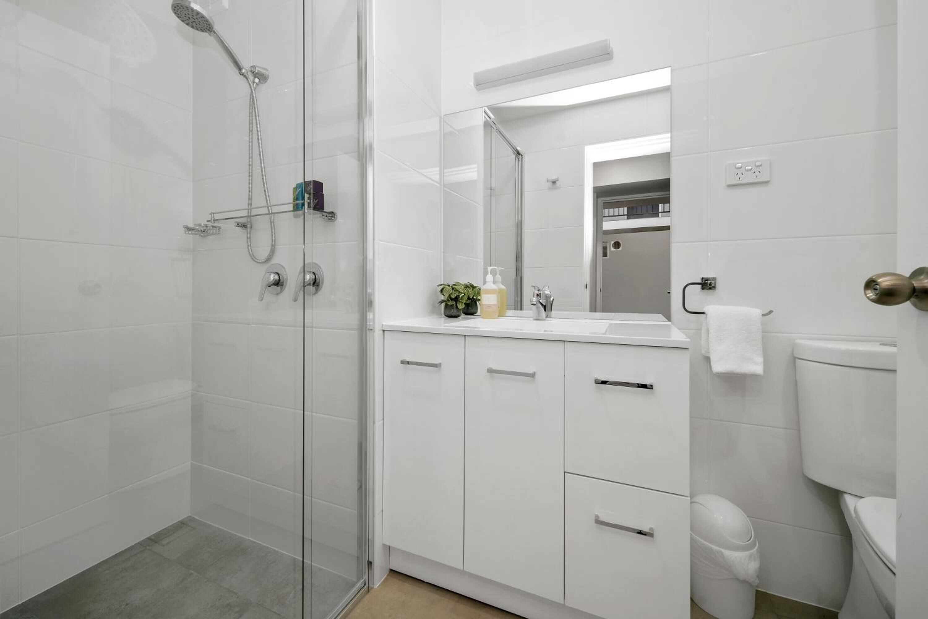 A modern bathroom with a glass shower enclosure, white cabinets, and a large mirror.