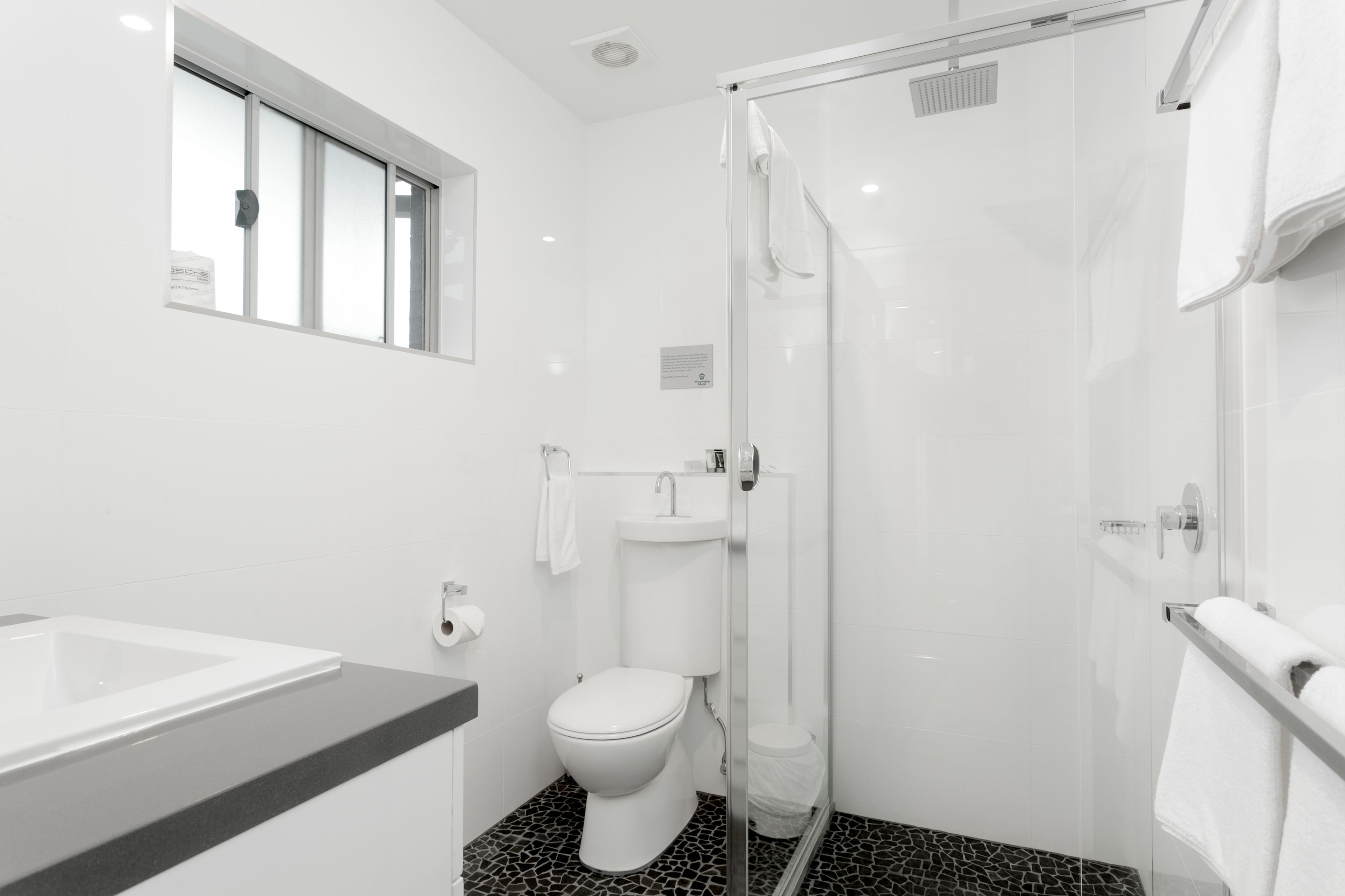 Un baño moderno con ducha acristalada, inodoro blanco y lavabo con encimera negra.