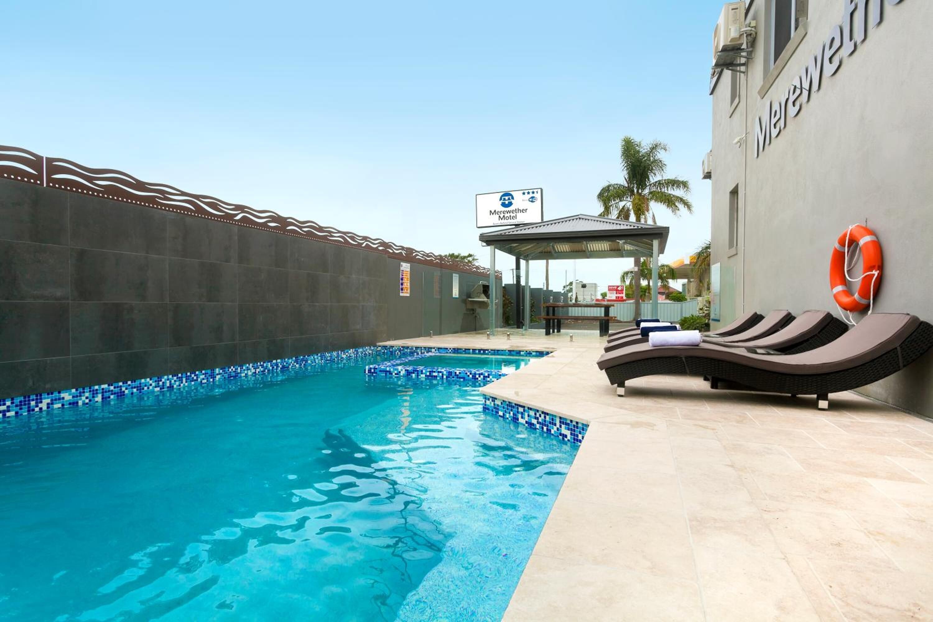 Une piscine dotée de chaises longues et d’une bouée de sauvetage, entourée d’un mur carrelé et d’un panneau indiquant le « Merrowet Motel ».