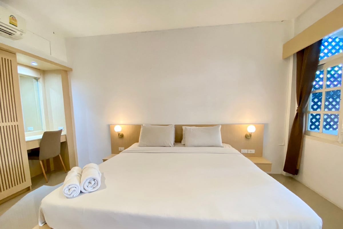 A hotel room with a large bed, two bedside tables, a desk with a chair, and a window with a lattice design.