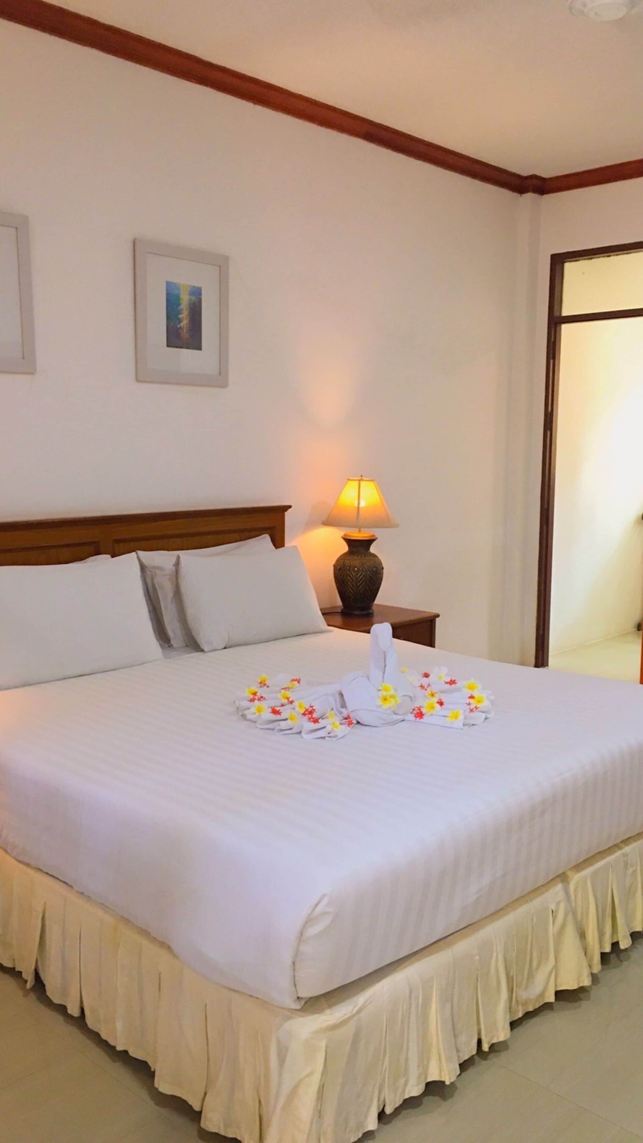 A neatly made bed with a white bedspread, a decorative towel, and a small table with a lamp beside it.
