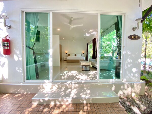 A modern hotel room with a glass door entrance, a ceiling fan, and a bed with a nightstand. - Garden Home Kata (Karon)