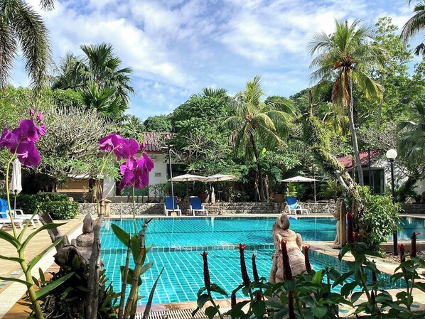 A pool area with lounge chairs and umbrellas, surrounded by tropical vegetation. - Garden Home Kata (Karon)
