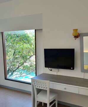 A room with a large window, a flat-screen TV mounted on the wall, a white desk, and a white chair. - Garden Home Kata (Karon)