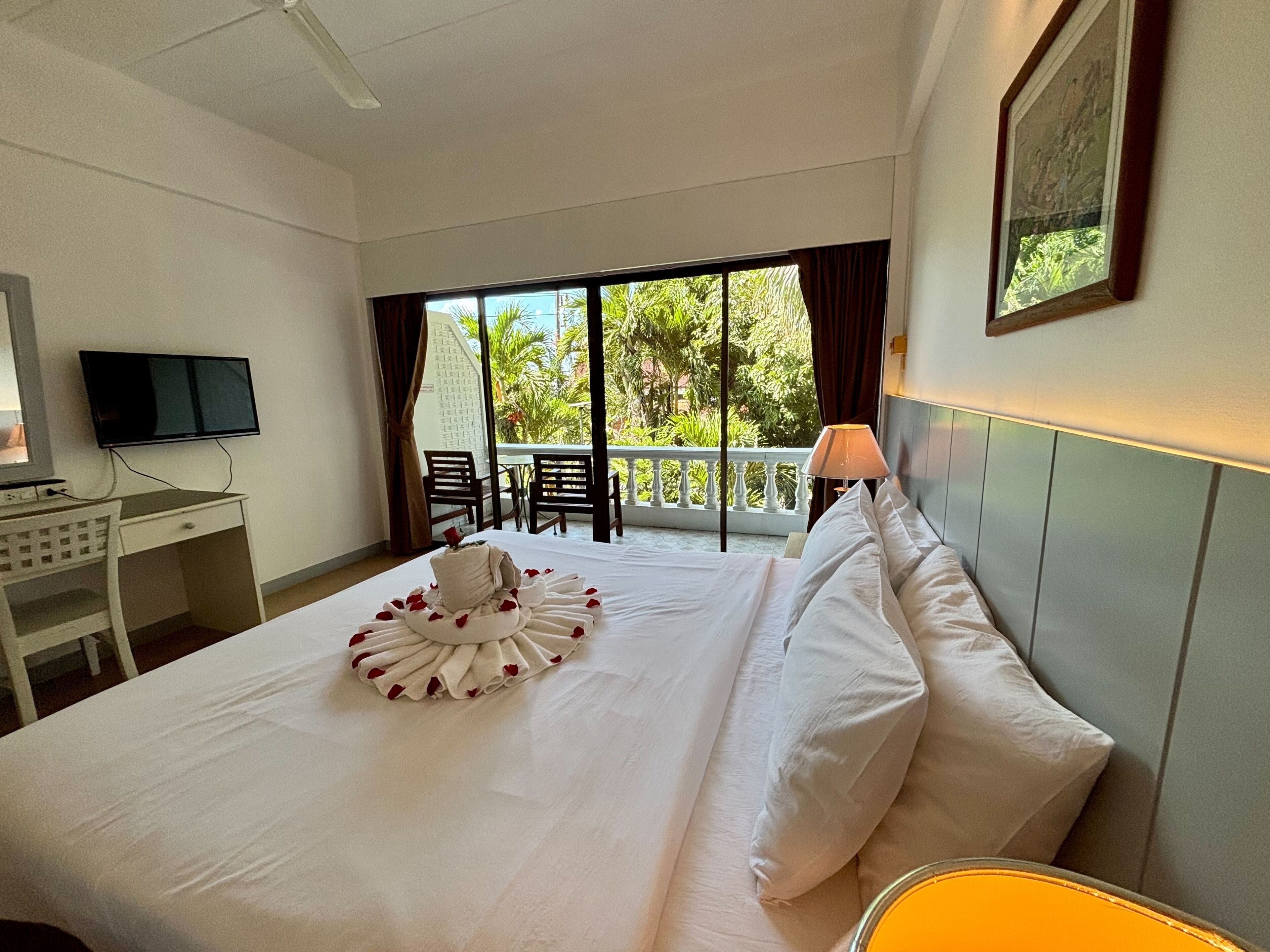 A hotel room with a bed, a desk, a television, and a balcony with chairs.