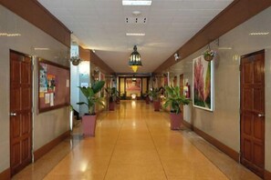 A hotel corridor with wooden doors, potted plants, and a central chandelier.