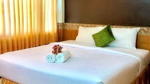 Una cama bien hecha con sábanas blancas, un almohadón verde y toallas enrolladas sobre la cama.