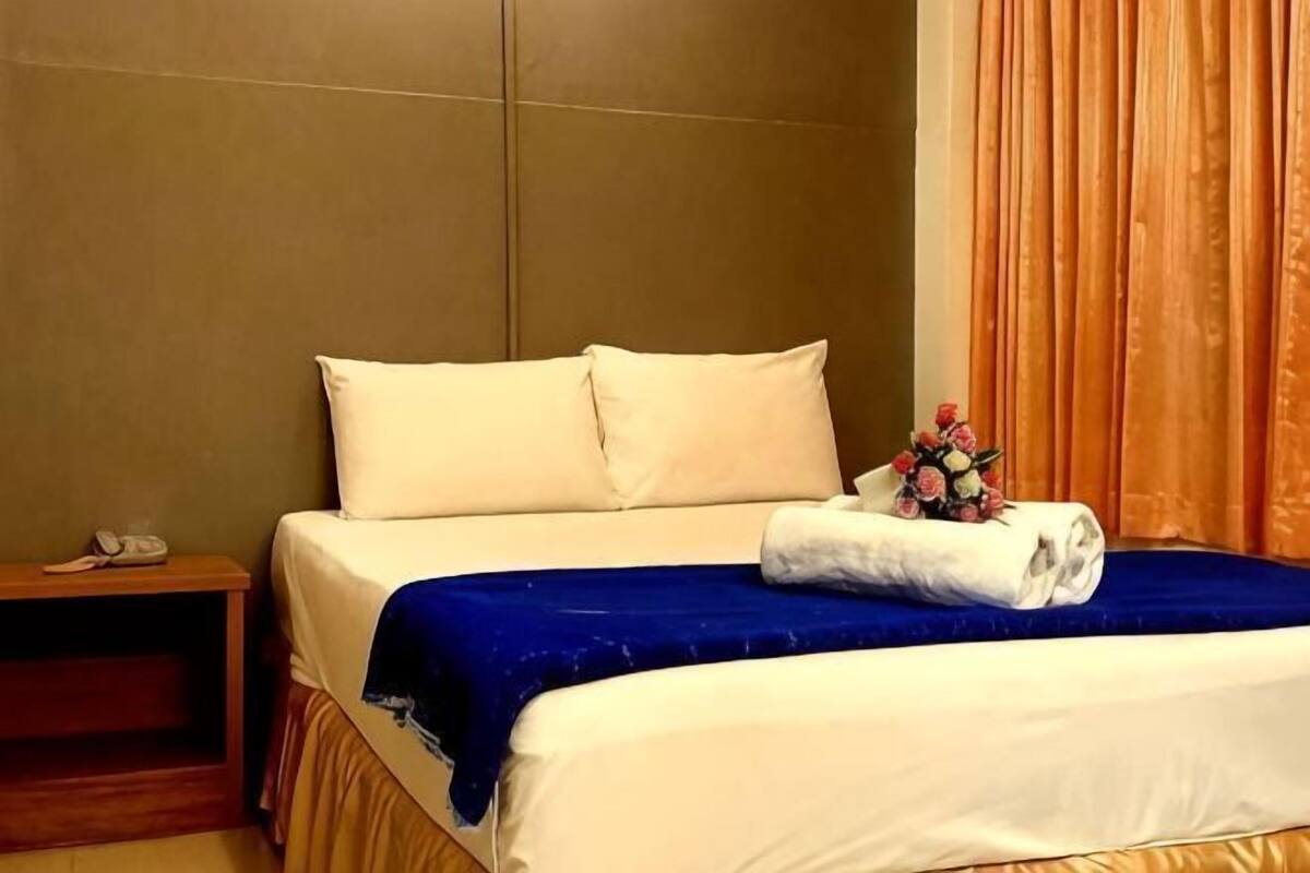 Una habitación de hotel con una cama, una mesita de noche, un teléfono y una cortina.