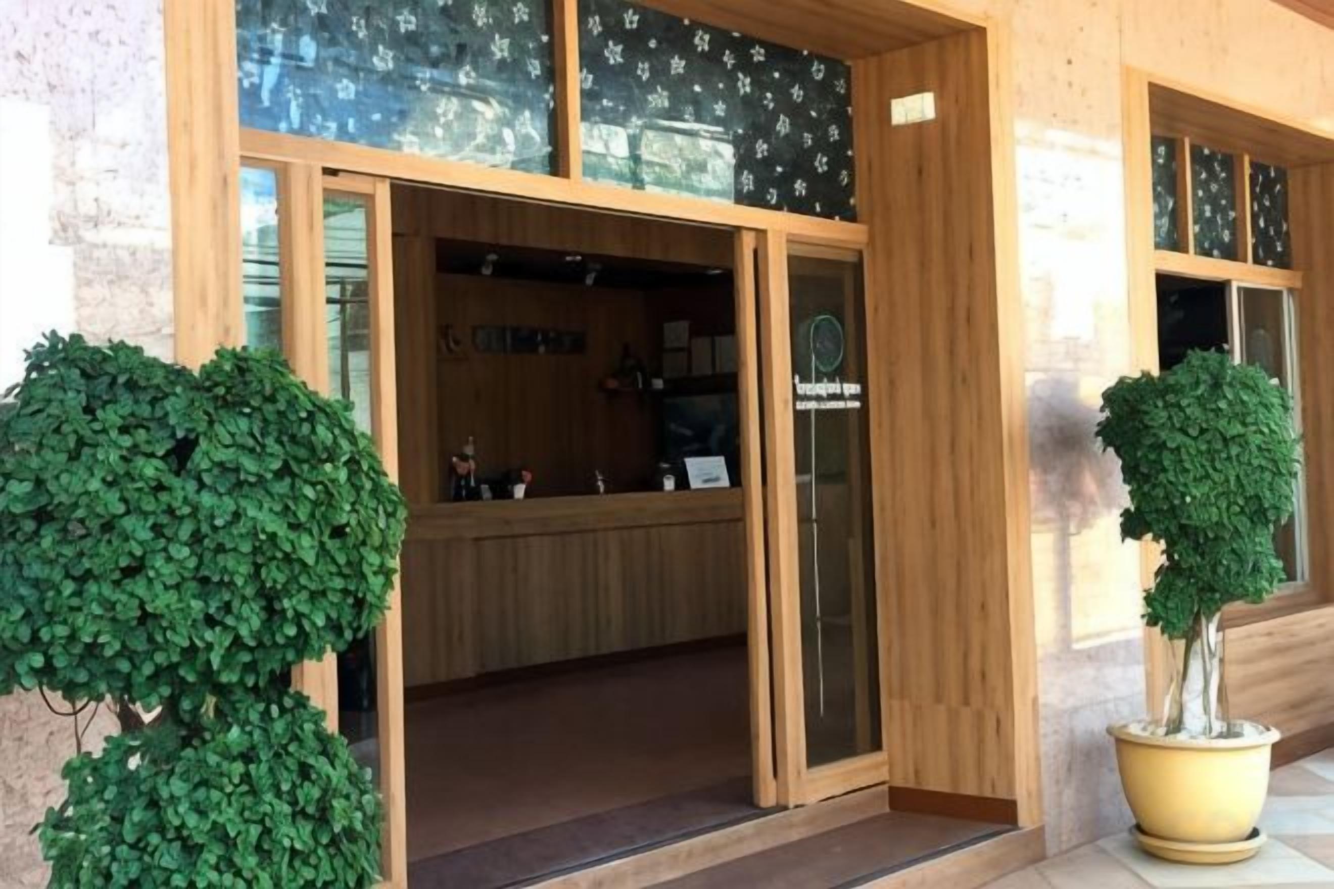 A hotel entrance with a reception desk, a potted tree, and a glass door.