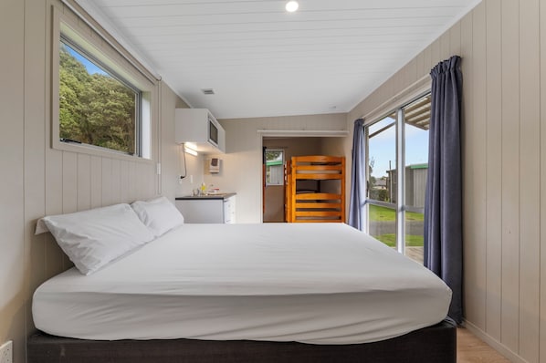 A bedroom with a large bed, a desk with a chair, a bunk bed, and a view of the outdoors. - Fitzroy Beach Holiday Park (New Plymouth)