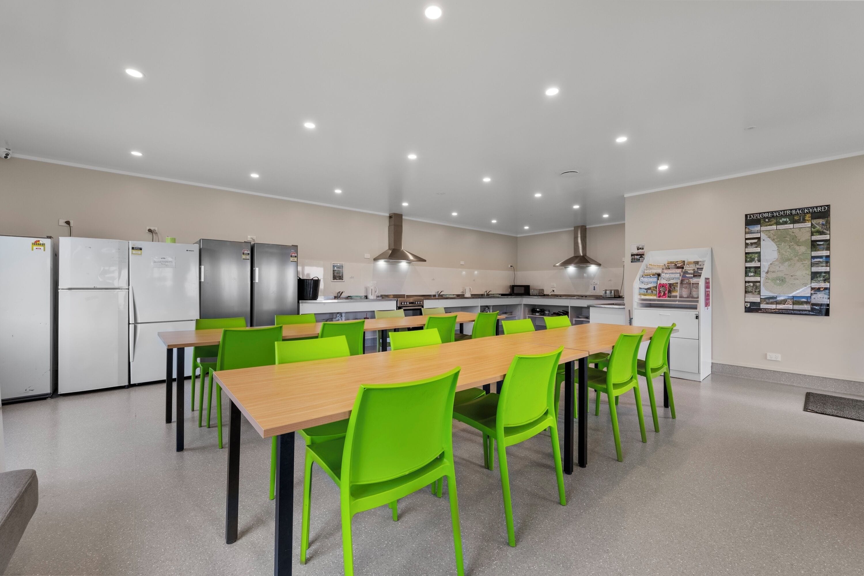 Una cocina moderna con electrodomésticos de acero inoxidable, una larga mesa de madera con sillas verdes y un mapa en la pared.