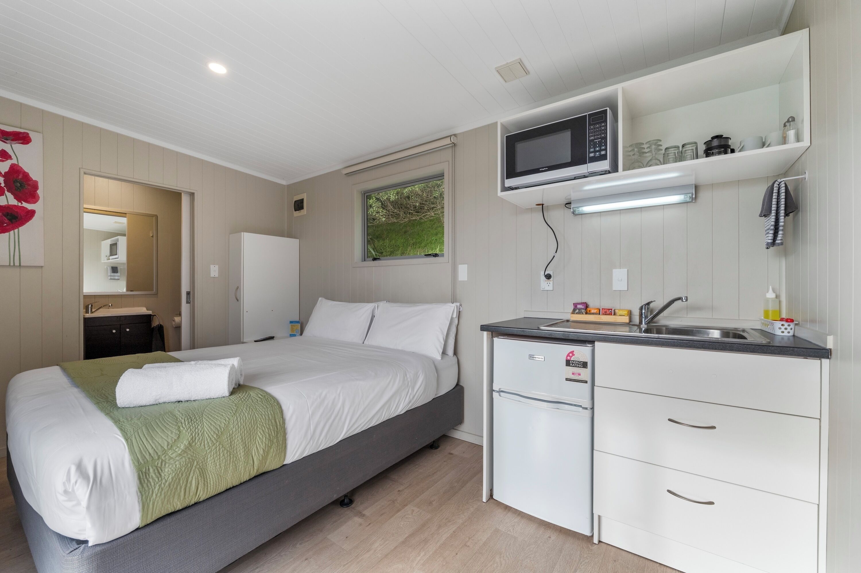 A modern bedroom with a bed, a small kitchenette, and a bathroom visible through an open door.