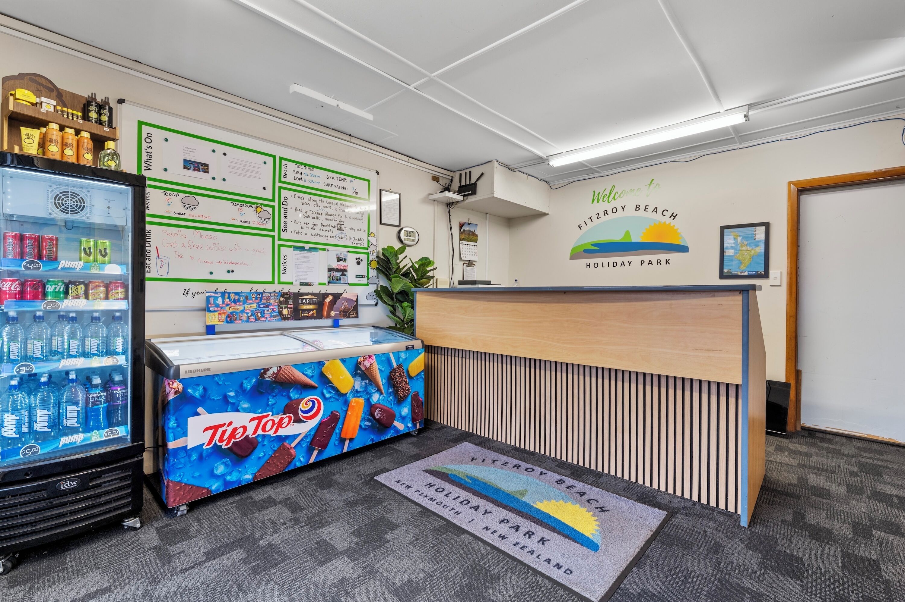A reception area with a counter, a refrigerator with beverages, a TipTop ice cream display, and informational posters on the wall.