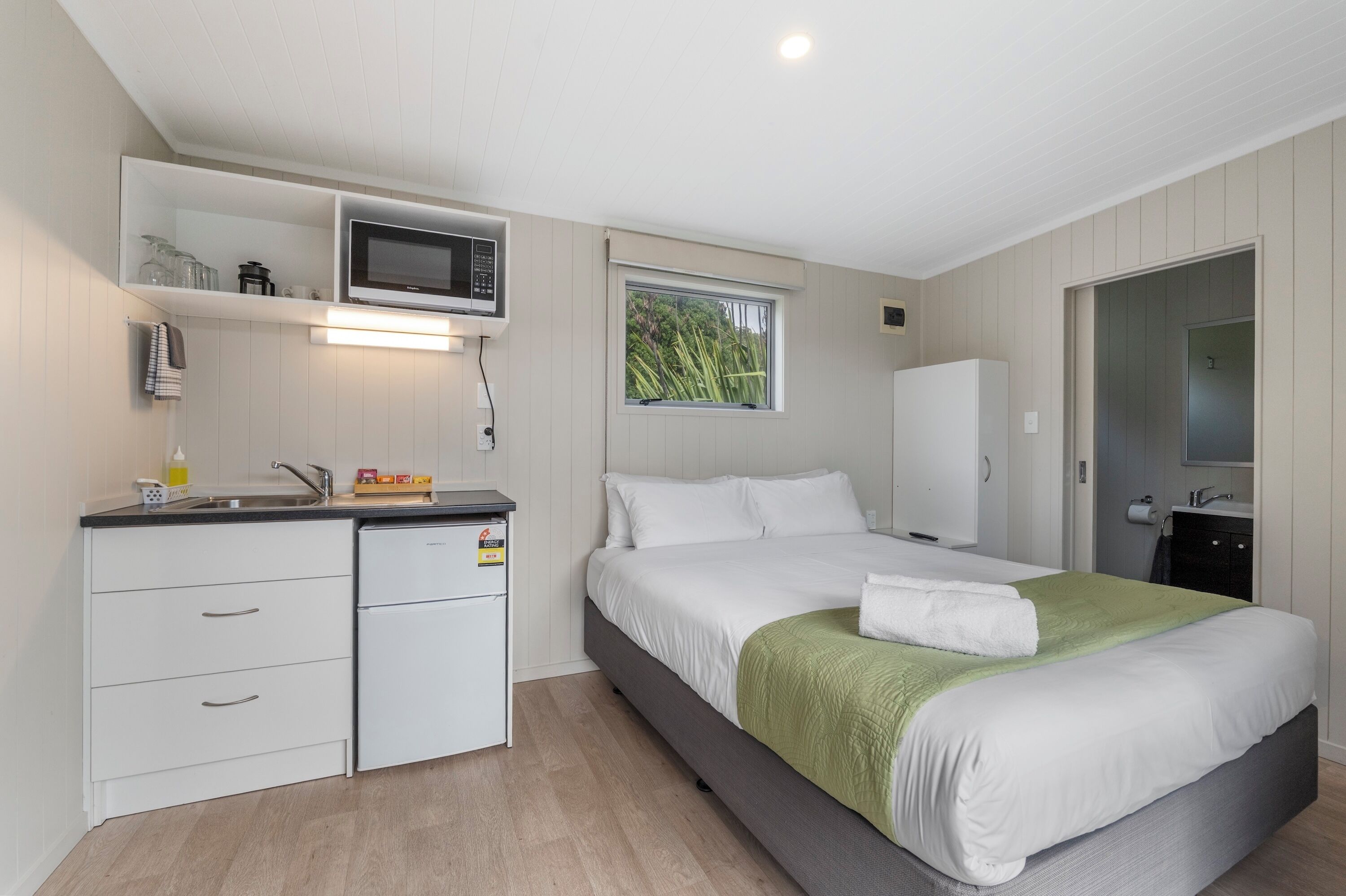 A modern bedroom with a bed, a small kitchenette, a window, and a door.
