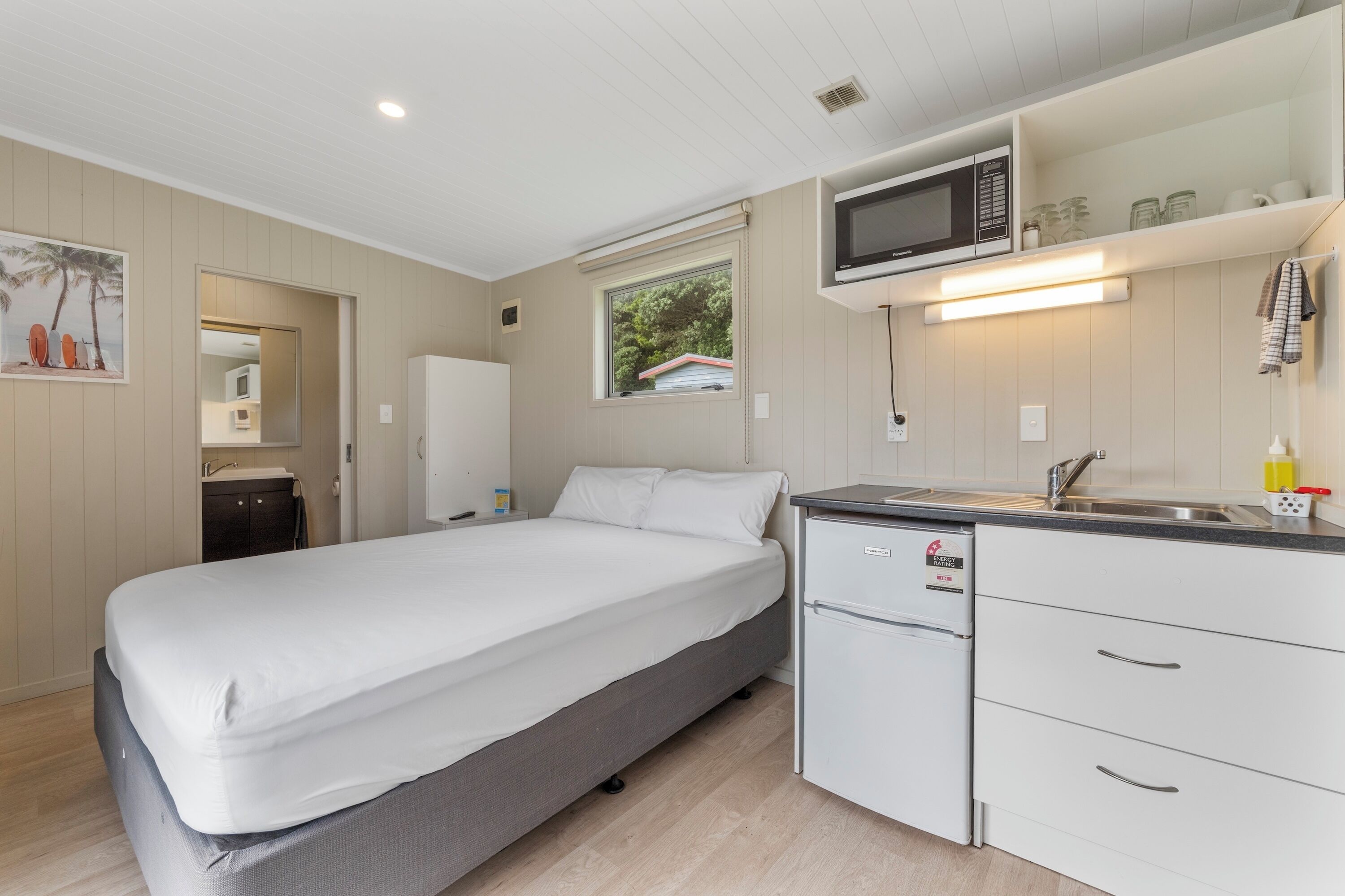 Une chambre compacte comprenant un lit, une petite kitchenette et une fenêtre donnant sur un espace verdoyant.