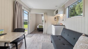 Een compacte kamer met een eettafel, een bank, een kleine kitchenette en een schuifdeur naar een tuin.