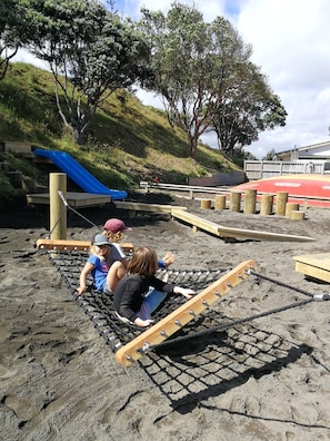 Explore the outdoor play area with a rope bridge and slide, surrounded by trees and a nearby building.