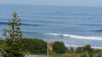 Um camping com tendas e um pequeno edifício, com vista para uma praia com ondas e surfistas.