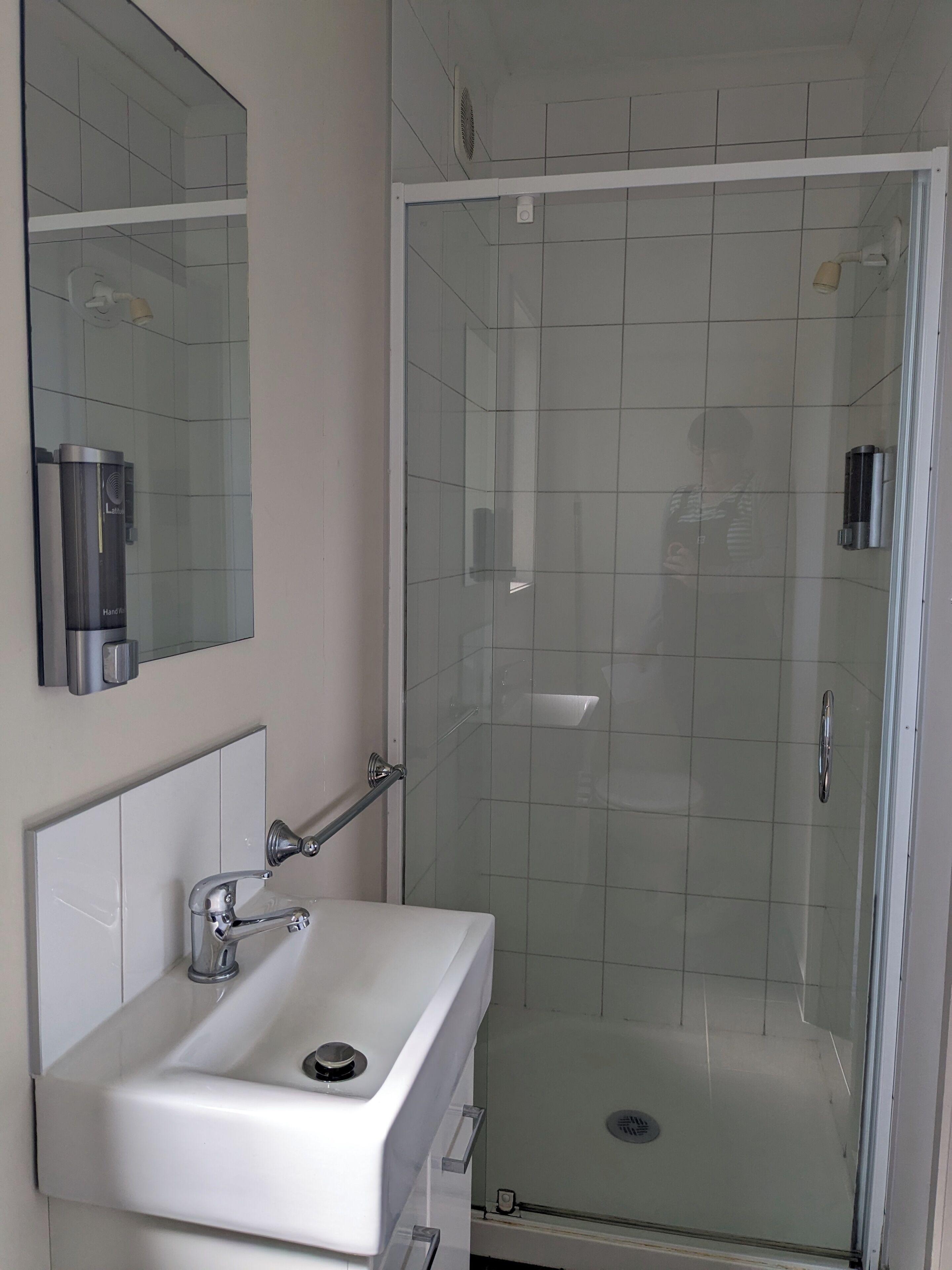 Un baño con un lavamanos blanco, un espejo y una ducha con mampara de vidrio.