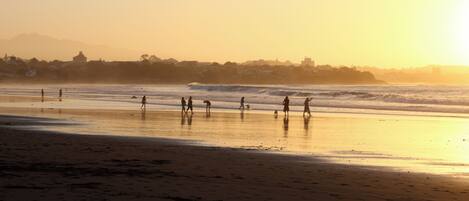 A beach with people walking and a sunset in the background.