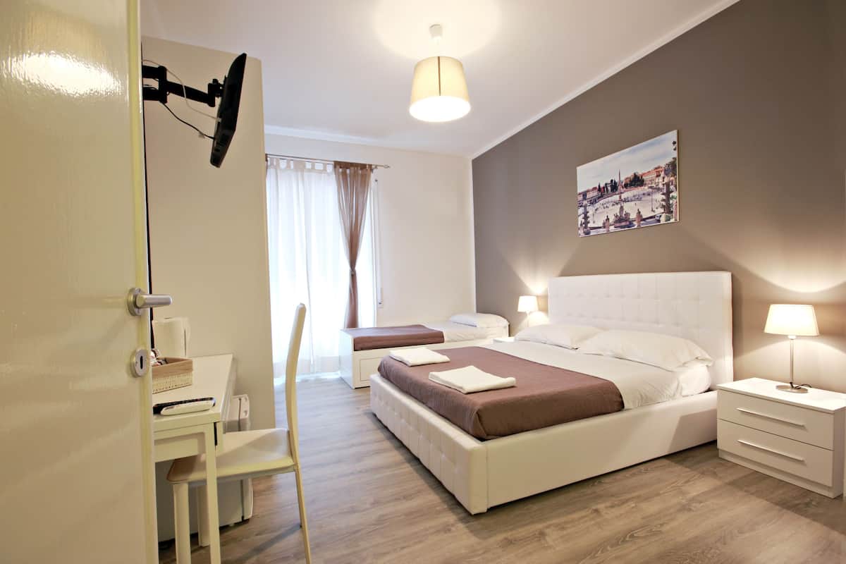A hotel room with two beds, a desk, a chair, and a nightstand with a lamp.