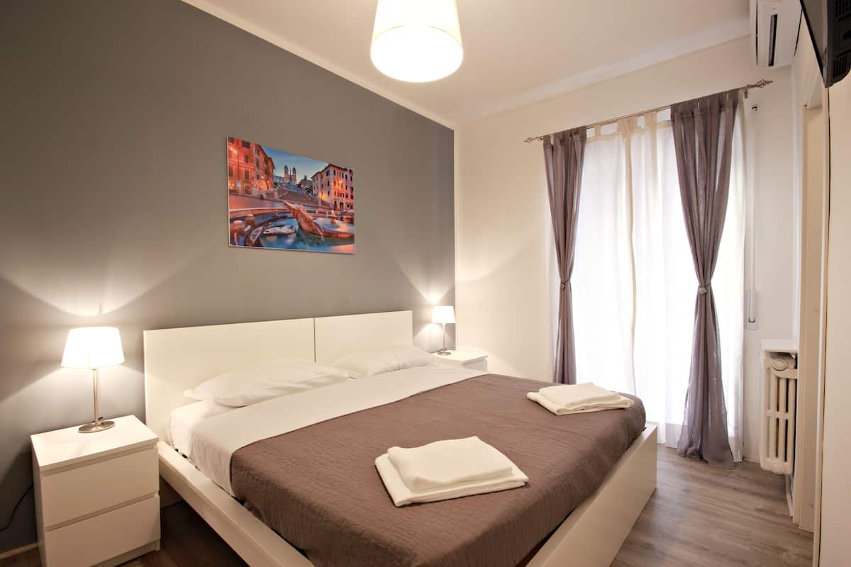 A neatly made bed with a brown bedspread, white pillows, and a white nightstand with a lamp.