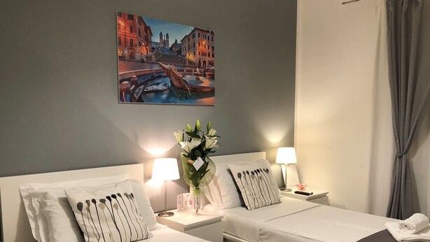 Une chambre d’hôtel avec deux lits, une table de chevet avec une lampe, un vase de fleurs et un tableau représentant un paysage urbain accroché au mur.