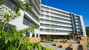 A modern multi-story building with a flat roof, large windows, and a courtyard with wooden planters and benches. - Deakin Residential Services (Burwood)