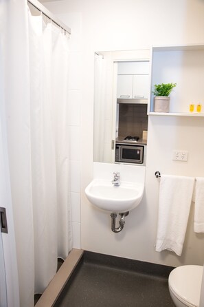 A bathroom with a shower, sink, toilet, and a microwave in the corner.