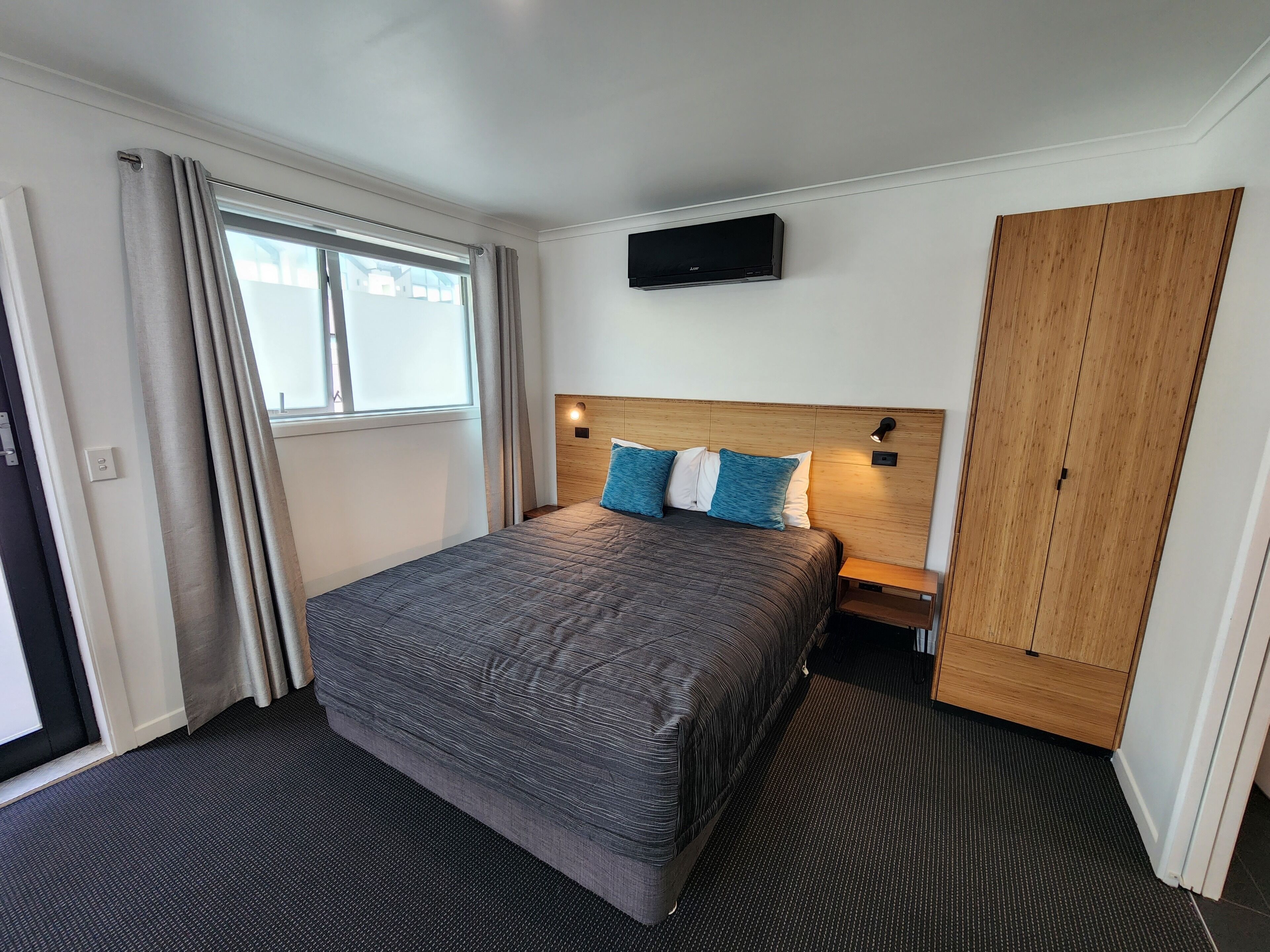Une chambre d’hôtel avec un lit, un téléviseur fixé au mur, une armoire et une fenêtre avec des rideaux.