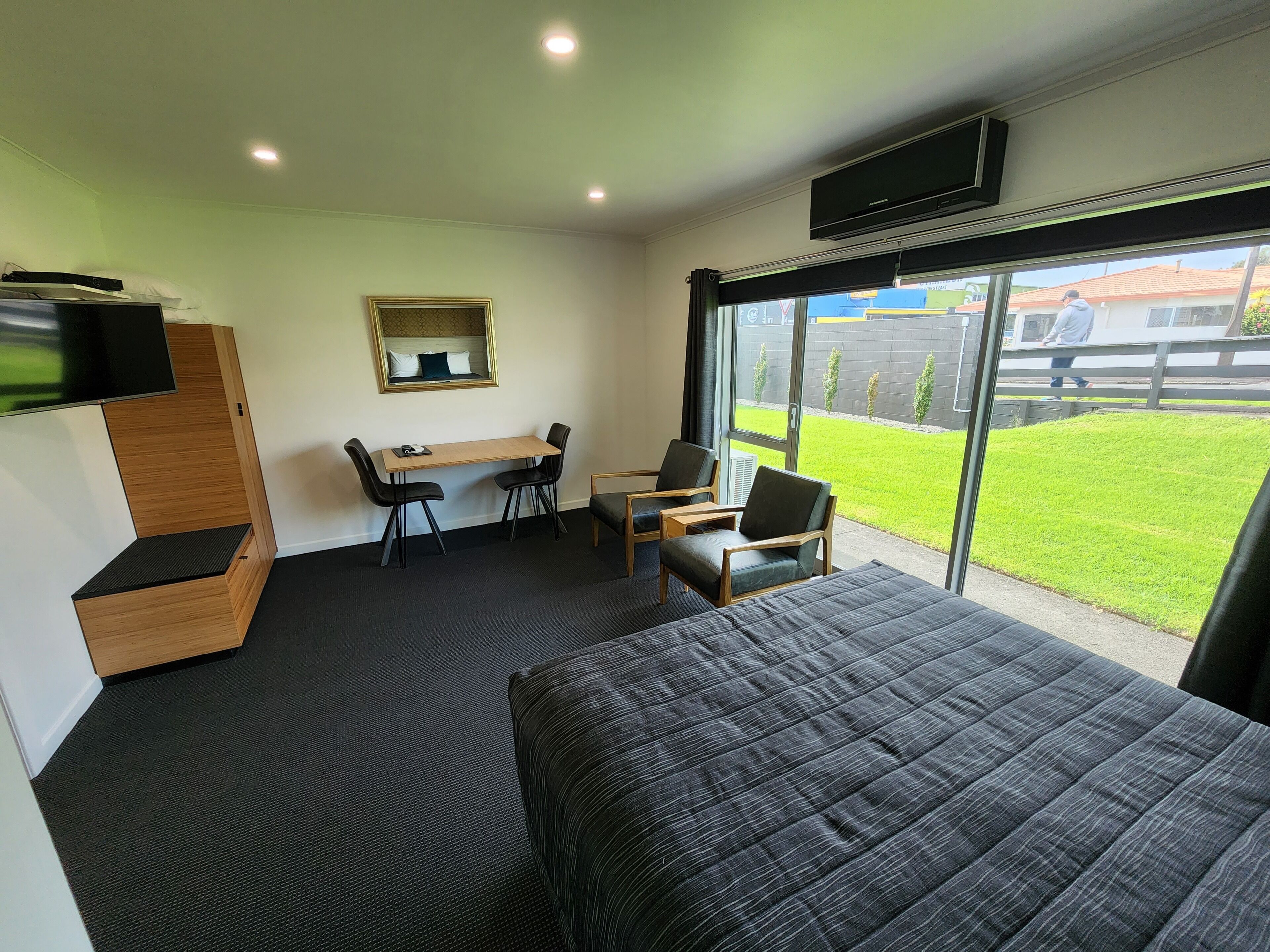 Una habitación de hotel con una cama, un escritorio con dos sillas, un televisor montado en la pared y un amplio ventanal con vistas al exterior.